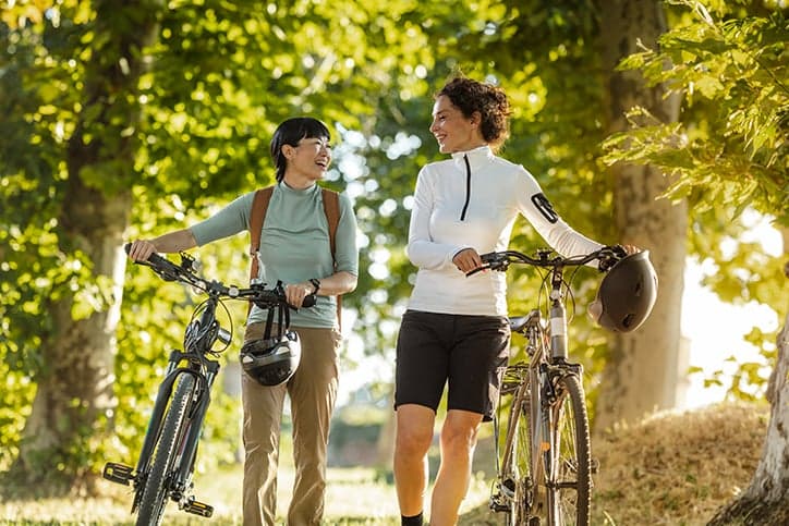 Two women walking through nature pushing their bikes