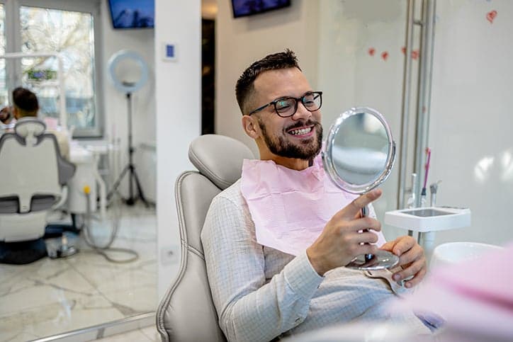 Man at the dentist, smiling into a mirror
